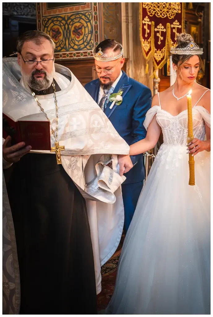 Priester führt Braut und Bräutigam mit Hochzeitskronen und Kerzen während der orthodoxen Trauungszeremonie um den Altar.