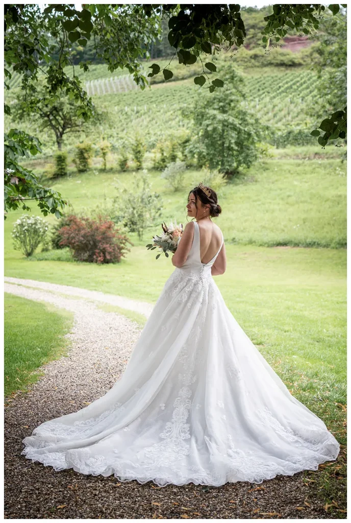 Braut steht mit langem Kleid auf einem Gartenweg