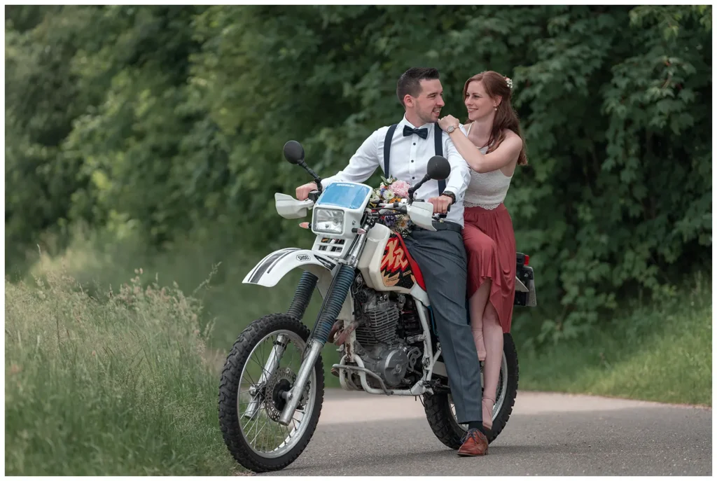 Brautpaar lehnt an einem Motorrad auf einer Landstraße